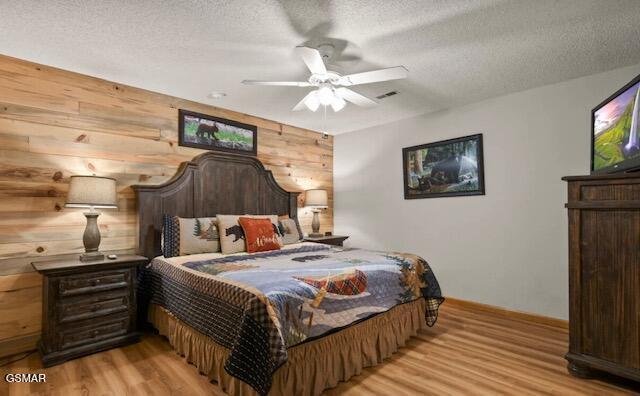 bedroom with a ceiling fan, light wood-type flooring, wooden walls, and a textured ceiling