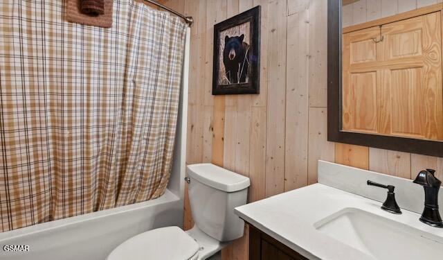 full bathroom featuring toilet, shower / tub combo, vanity, and wooden walls