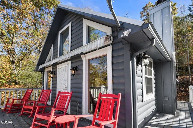 view of side of property featuring a deck, log veneer siding, and a chimney