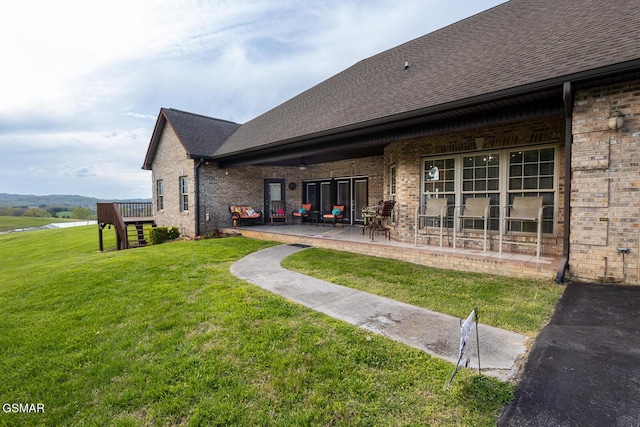 back of property with brick siding, a shingled roof, a patio area, and a lawn