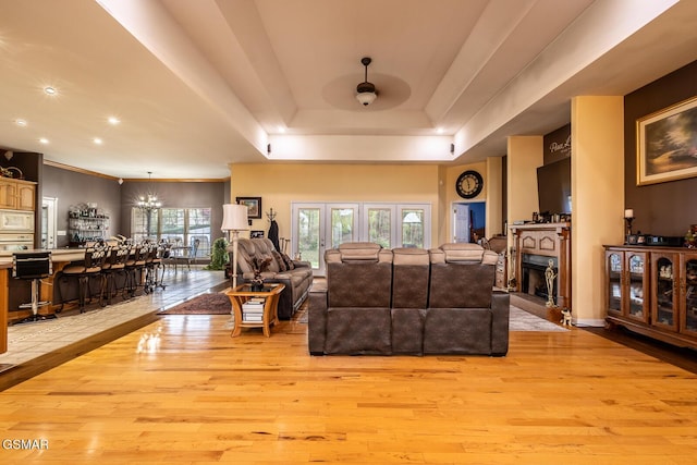 living area with ceiling fan, light wood finished floors, a raised ceiling, and a fireplace