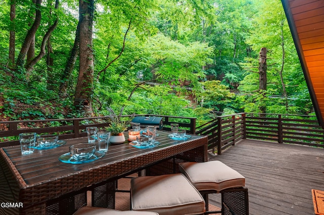 view of wooden balcony featuring outdoor dining space, a wooded view, and a wooden deck