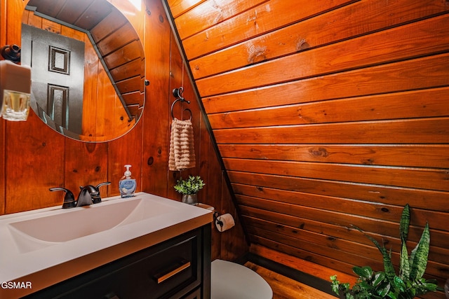 half bathroom featuring wood walls, vanity, and toilet
