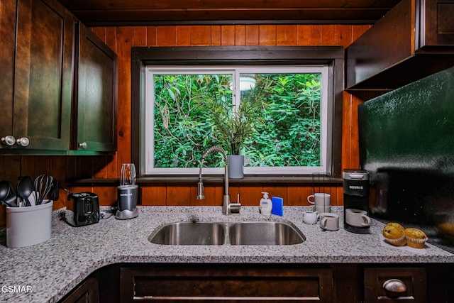 kitchen featuring wood walls, light stone counters, plenty of natural light, and a sink