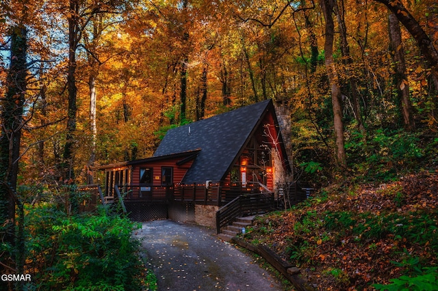view of front facade featuring a wooden deck, a shingled roof, stairway, and a forest view