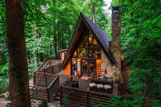 rear view of house featuring a deck, faux log siding, stone siding, and french doors