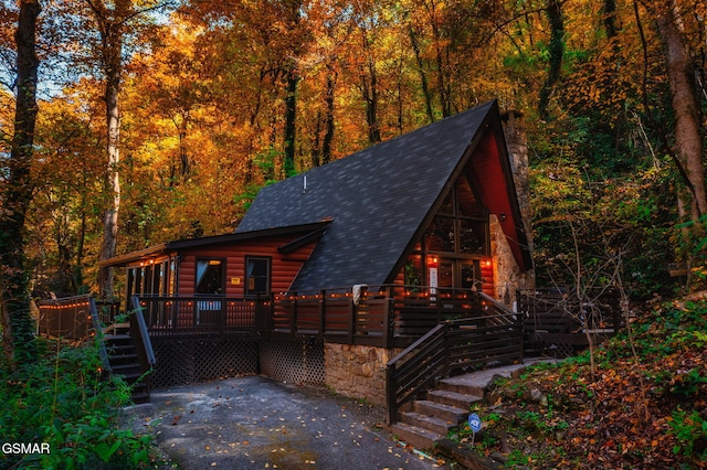 view of front of property with a deck, stairway, a wooded view, and roof with shingles