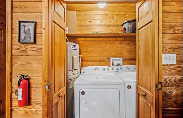 laundry area with electric water heater, washing machine and clothes dryer, and wooden walls