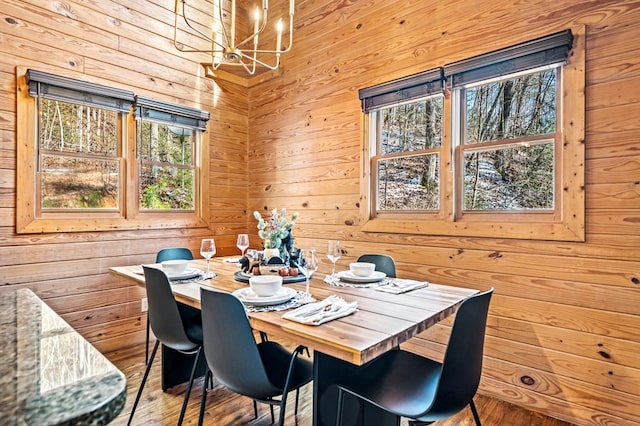 dining space featuring wood-type flooring, wooden walls, and an inviting chandelier