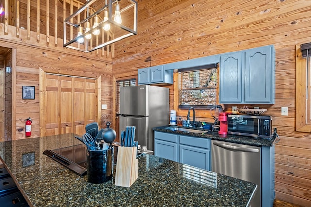 kitchen with decorative light fixtures, stainless steel appliances, wooden walls, sink, and blue cabinetry