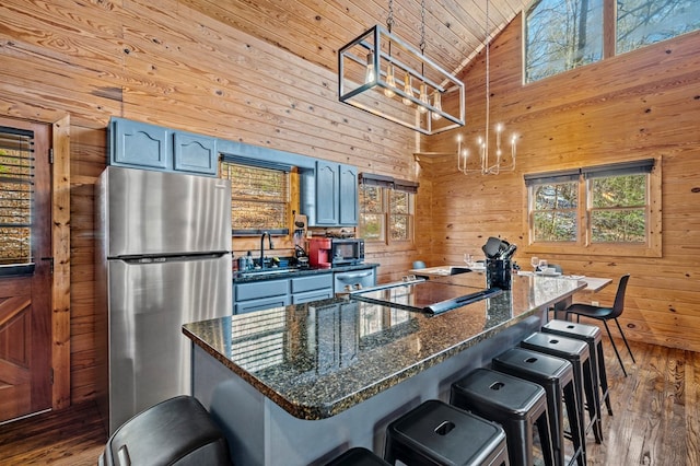 kitchen featuring stainless steel fridge, wooden walls, hanging light fixtures, a breakfast bar, and sink