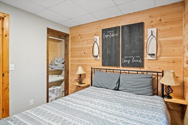 bedroom with a paneled ceiling and wood walls