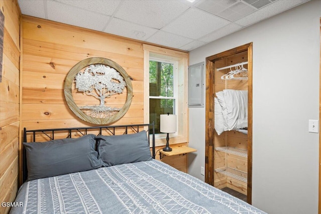 bedroom featuring a paneled ceiling, wooden walls, and electric panel