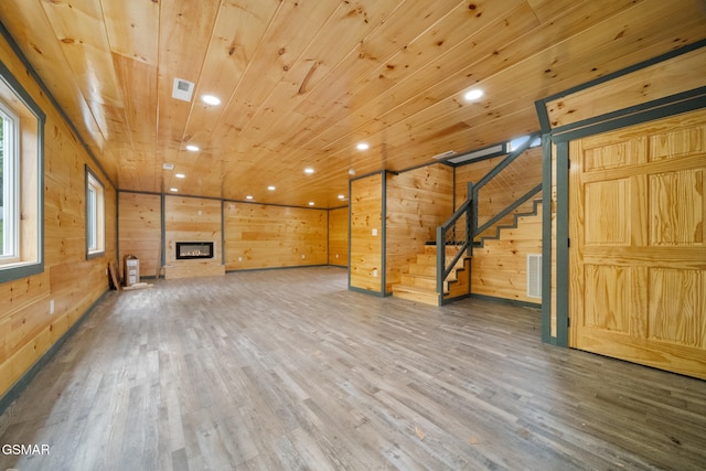 unfurnished living room with a glass covered fireplace, wood finished floors, wood walls, stairway, and wooden ceiling