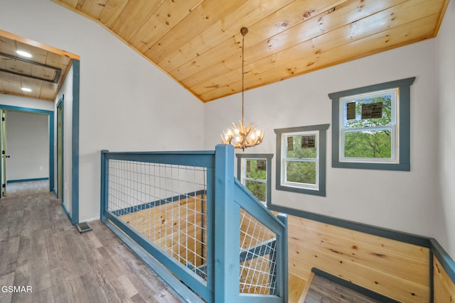 hallway with vaulted ceiling, wood finished floors, an inviting chandelier, wooden ceiling, and baseboards