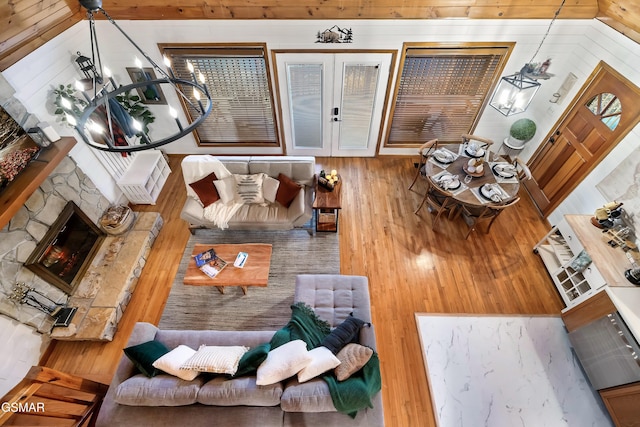 living area featuring a chandelier, a stone fireplace, wooden walls, and wood finished floors