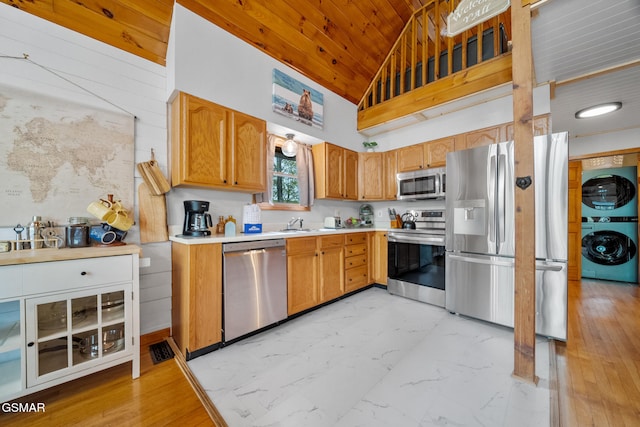 kitchen with stacked washer and dryer, stainless steel appliances, wooden ceiling, light countertops, and high vaulted ceiling