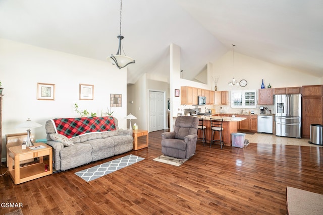 living room featuring high vaulted ceiling, wood-type flooring, sink, and a chandelier