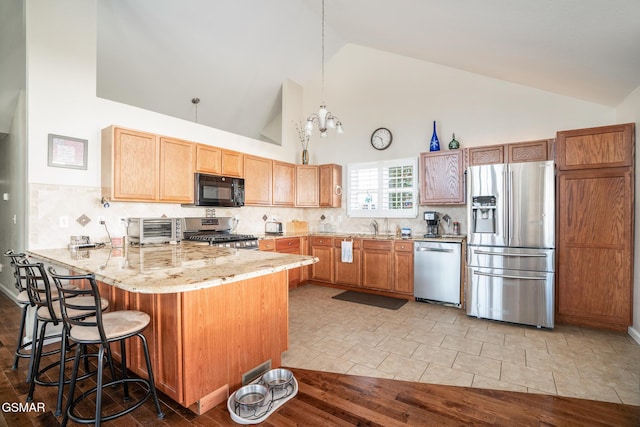 kitchen with a kitchen bar, kitchen peninsula, appliances with stainless steel finishes, hanging light fixtures, and high vaulted ceiling