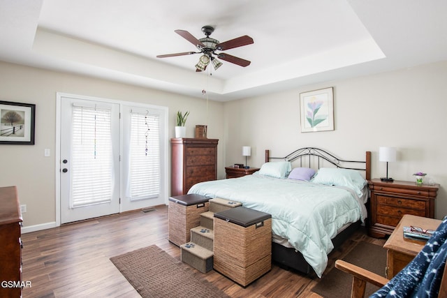 bedroom with dark wood-type flooring, ceiling fan, and a tray ceiling