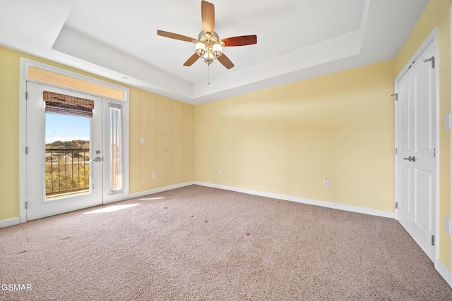 carpeted spare room featuring a tray ceiling and ceiling fan