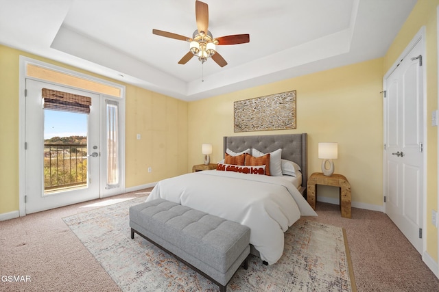 bedroom with ceiling fan, light carpet, access to outside, and a tray ceiling