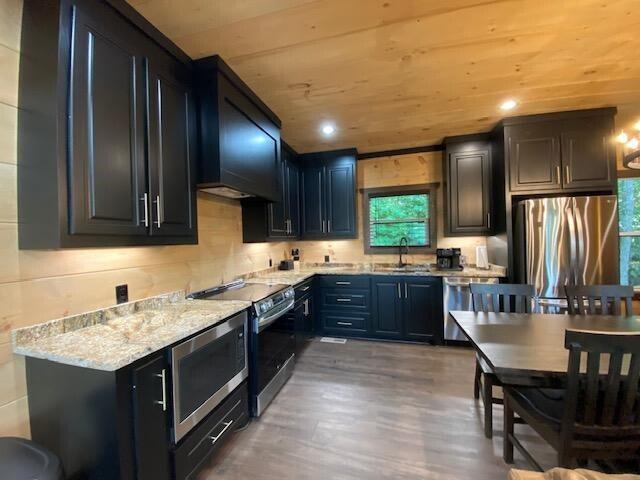 kitchen with light stone countertops, appliances with stainless steel finishes, dark hardwood / wood-style floors, wooden ceiling, and range hood