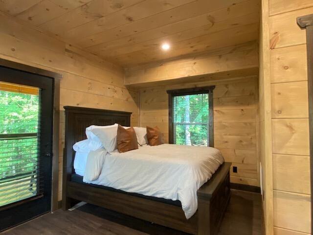 bedroom with dark hardwood / wood-style flooring, access to outside, wood ceiling, and wooden walls