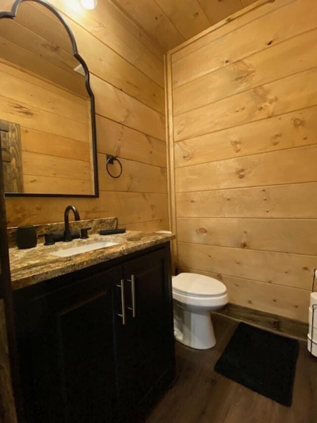 bathroom featuring toilet, vanity, wood-type flooring, and wood walls