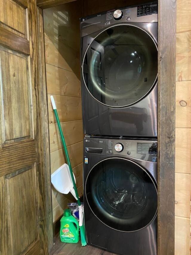 washroom with stacked washer and dryer, wood walls, and hardwood / wood-style flooring