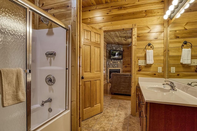 bathroom with vanity, shower / bath combination with glass door, wooden ceiling, a stone fireplace, and wooden walls