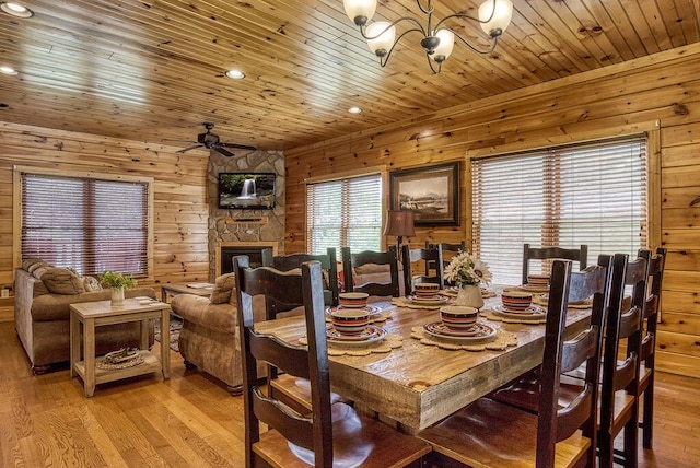 dining area featuring wooden walls, ceiling fan, a fireplace, light hardwood / wood-style floors, and wood ceiling