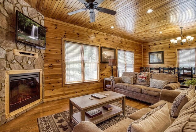 living room featuring light wood-type flooring, ceiling fan with notable chandelier, a stone fireplace, and wood ceiling