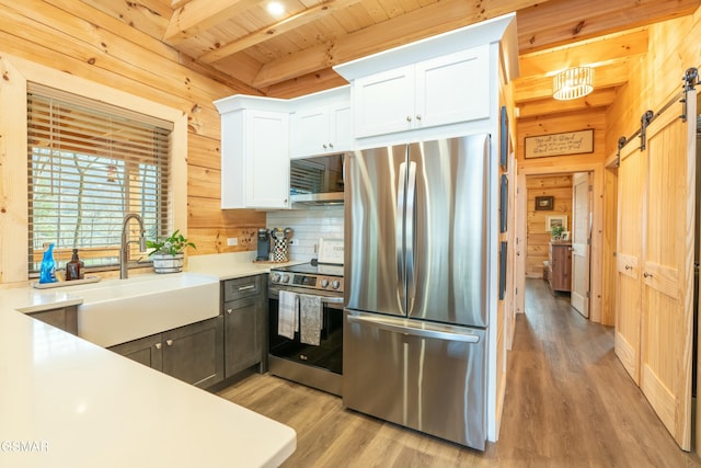 kitchen with a barn door, wood ceiling, stainless steel appliances, wood walls, and a sink