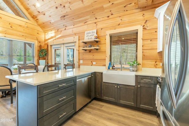 kitchen featuring wooden walls, lofted ceiling, a peninsula, stainless steel appliances, and a sink