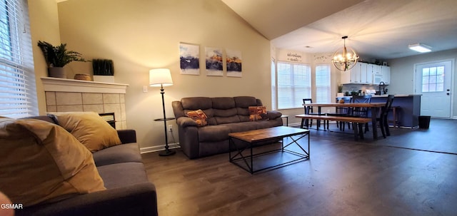 living area featuring lofted ceiling, a notable chandelier, dark wood-style flooring, baseboards, and a tiled fireplace