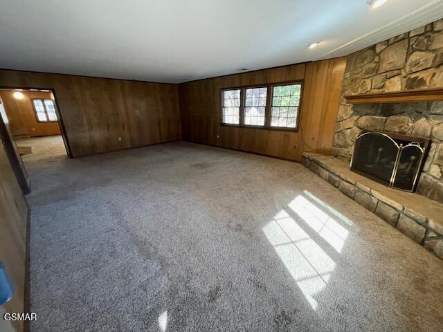 unfurnished living room with light colored carpet, a fireplace, and wooden walls