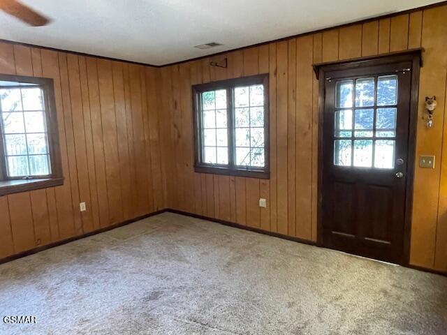 foyer with carpet floors, ceiling fan, and wooden walls