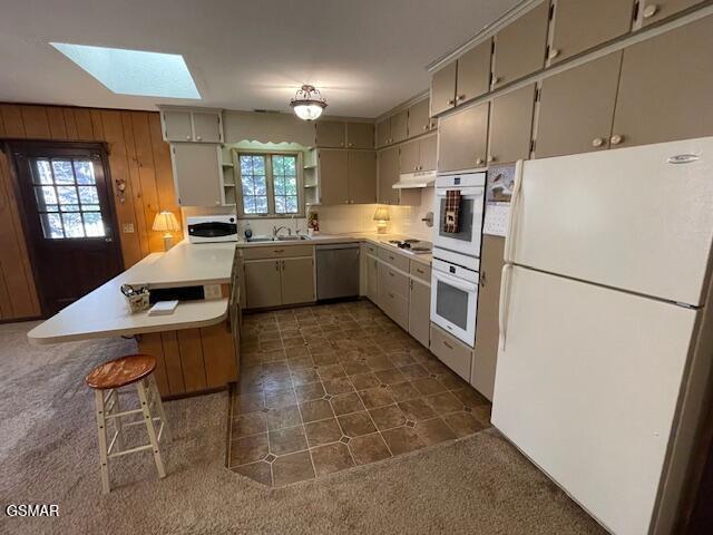 kitchen featuring a breakfast bar, white appliances, a skylight, and a wealth of natural light