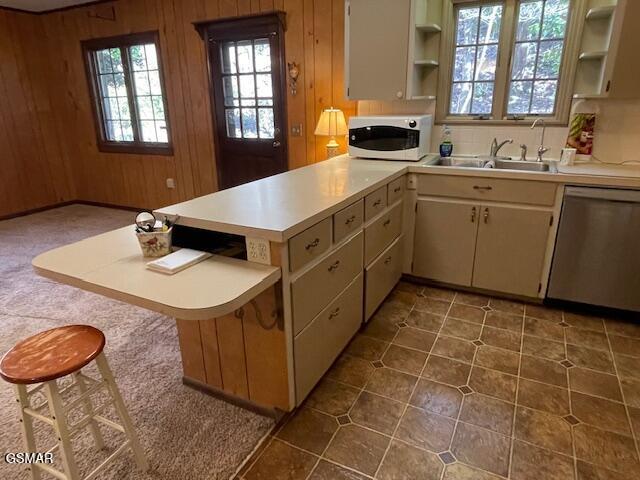 kitchen featuring dishwasher, wooden walls, plenty of natural light, kitchen peninsula, and a breakfast bar