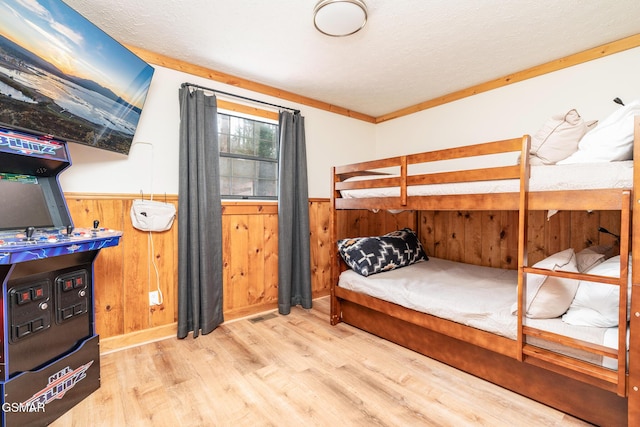 bedroom with crown molding, wooden walls, and light hardwood / wood-style flooring