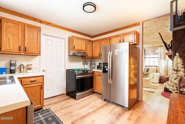 kitchen with sink, crown molding, light hardwood / wood-style floors, wooden walls, and appliances with stainless steel finishes