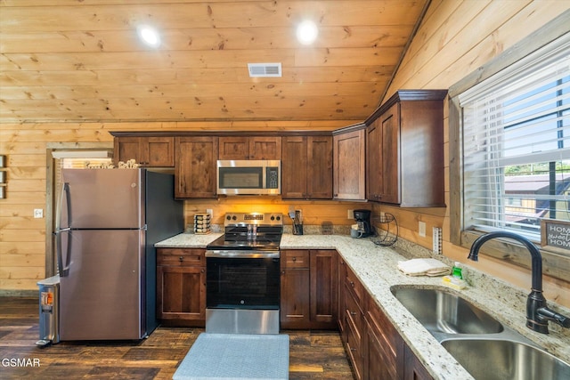 kitchen with sink, light stone counters, wooden walls, dark hardwood / wood-style flooring, and stainless steel appliances