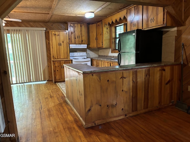 kitchen with wooden walls, kitchen peninsula, black fridge, dark wood-type flooring, and electric stove