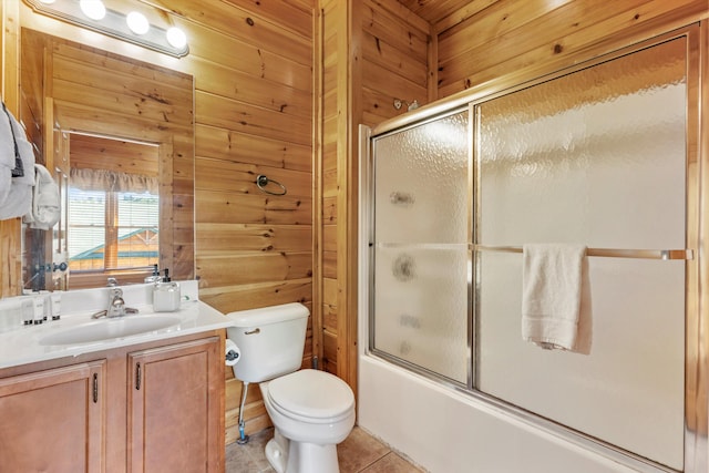 full bath featuring tile patterned floors, toilet, vanity, wooden walls, and bath / shower combo with glass door