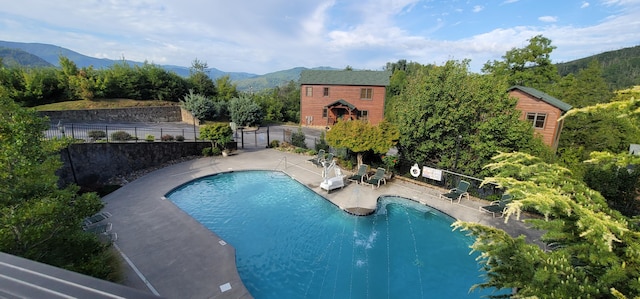 community pool featuring a mountain view, fence, and a patio
