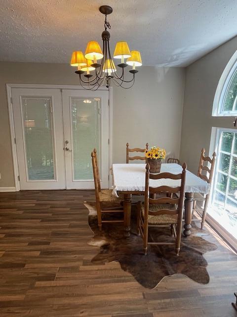 dining space with french doors, dark hardwood / wood-style floors, a textured ceiling, and an inviting chandelier