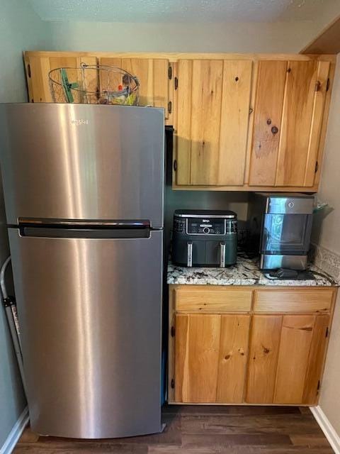 kitchen with light stone counters, dark wood-type flooring, and stainless steel refrigerator