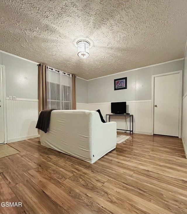 unfurnished living room featuring a wainscoted wall, a textured ceiling, wood finished floors, and ornamental molding