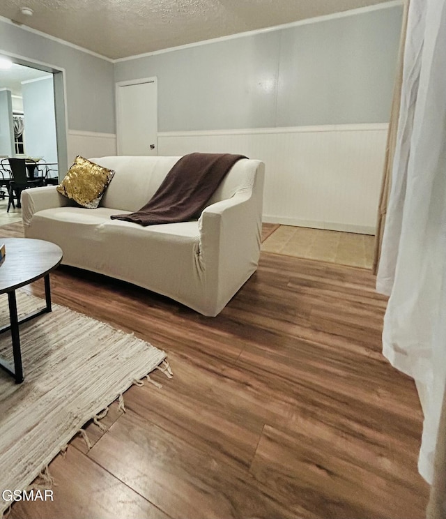 living room featuring a textured ceiling, wood finished floors, wainscoting, and crown molding